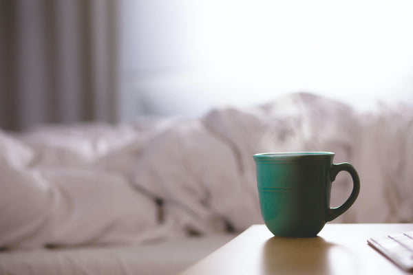A cup of hot tea or herbs next to a bed, Natural Sleep Remedy header image